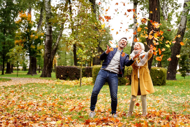 Happy married Couple having fun together outdoor in the golden autumn park, throwing leaves and laughing. Wife and husband in love. Real people emotions concept. - Photo, image