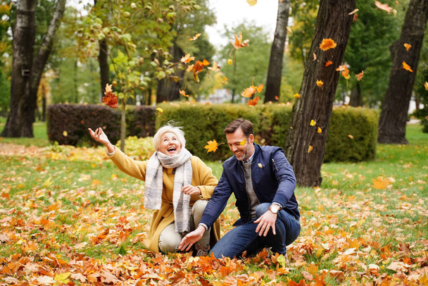 Happy handsome couple enjoying the beautiful autumn day in park, haivng fun together, throwing golden leaves and laughing. Real people lifestyle - Photo, Image