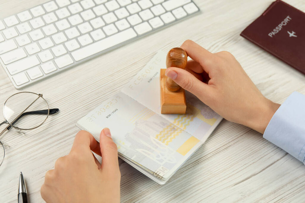 Moldova, Ceadir-Lunga - June 13, 2022: Woman stamping visa page in passport at white wooden table, closeup - Fotó, kép