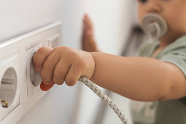 Cute baby playing with plug and electrical socket at home, closeup. Dangerous situation - Фото, зображення
