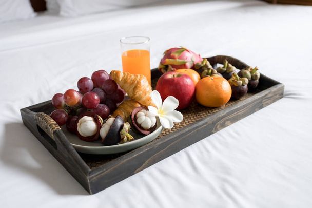 Breakfast, fruit, croissants, orange juice, in a black wooden tray, on a white bedsheet, Healthy food concept. - Photo, image