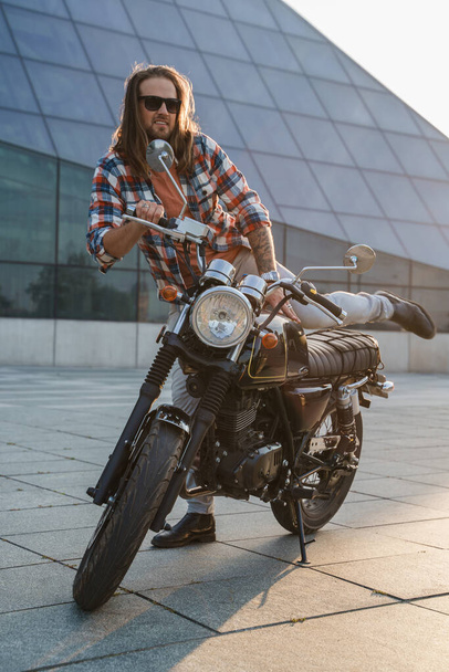Aufnahme von stilvollem Mann Biker mit Bart und Sonnenbrille auf seinem Motorrad. - Foto, Bild