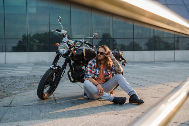 Portrait of cool guy biker with sunglasses sitting on asphalt. - Photo, Image