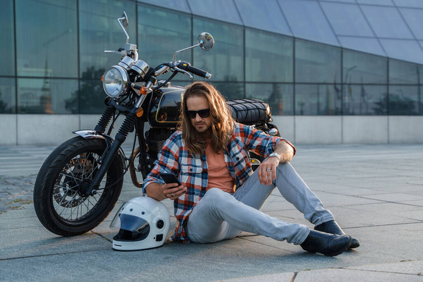 Portré szakállas férfi motoros egyéni motorkerékpár pózol aszfalton. - Fotó, kép