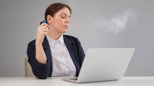 Business woman smoking a disposable vape while sitting at her desk - Фото, зображення