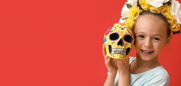 Little girl with painted human skull on red background. Celebration of Mexico's Day of the Dead (El Dia de Muertos) - Photo, Image