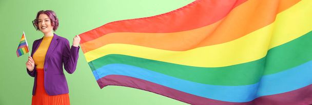 Young woman with LGBT flags on green background - Фото, изображение