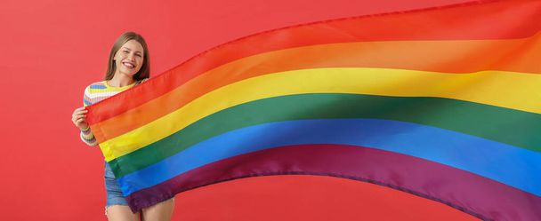 Kırmızı arka planda LGBT bayrağı olan genç bir kadın. - Fotoğraf, Görsel