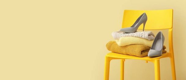 Stuhl mit Stapel stylischer Pullover und Damenschuhe auf gelbem Hintergrund mit Platz für Text - Foto, Bild