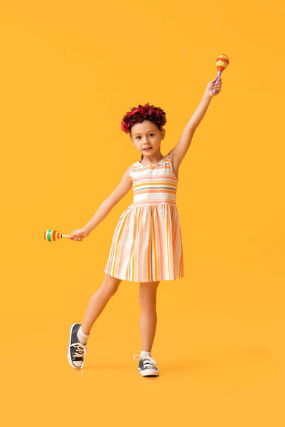 Little Mexican girl with floral wreath and maracas on yellow background - Foto, Imagem