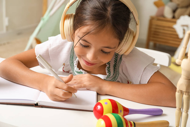 Petite Mexicaine avec écouteurs faisant des devoirs à la maison - Photo, image