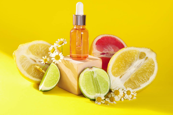 Composição com garrafa de óleo essencial, frutas cítricas e flores de camomila sobre fundo amarelo - Foto, Imagem