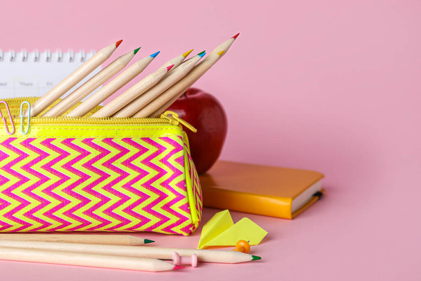 Case with pencils, paper plane, apple and calendar on pink background - Fotografie, Obrázek