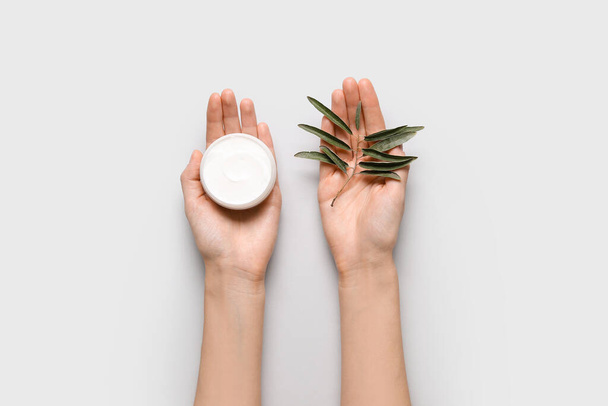 Manos femeninas con frasco de crema de oliva natural y rama de planta sobre fondo blanco, primer plano - Foto, imagen