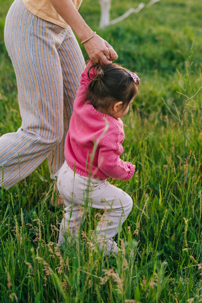 Anne bebek elini tutuyor, sonbahar günü parkta yürüyor. Mutlu aile, çocukluk. Çocuk bakımı. Ebeveyn, çocuk. Yaz doğası. Doğa Ana. Yeşil doğa. - Fotoğraf, Görsel