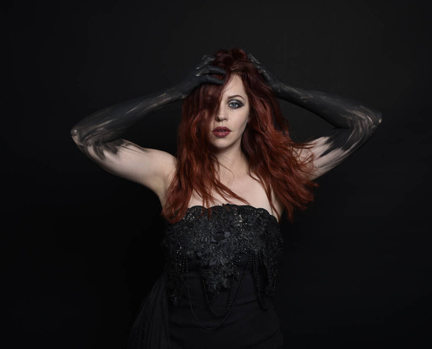 közeli portré gyönyörű nő vörös hajú, visel fekete ruhát elegáns gesztusos kéz pózol egy sötét stúdió háttér hangulatos világítás. - Fotó, kép