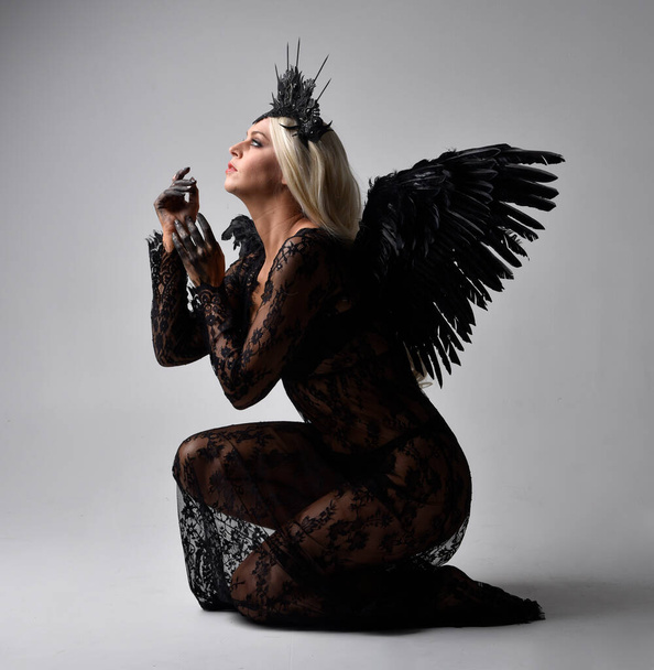 頭部と羽の天使の翼を持つ黒いゴシック様式のドレスを身に着けている美しいモデルの肖像画。スタジオの背景に隔離され. - 写真・画像