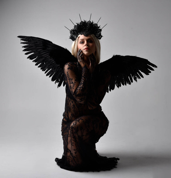 portrait of beautiful  model  wearing black gothic dress with headdress  and feathered angel wings.  isolated on studio background. - Photo, Image