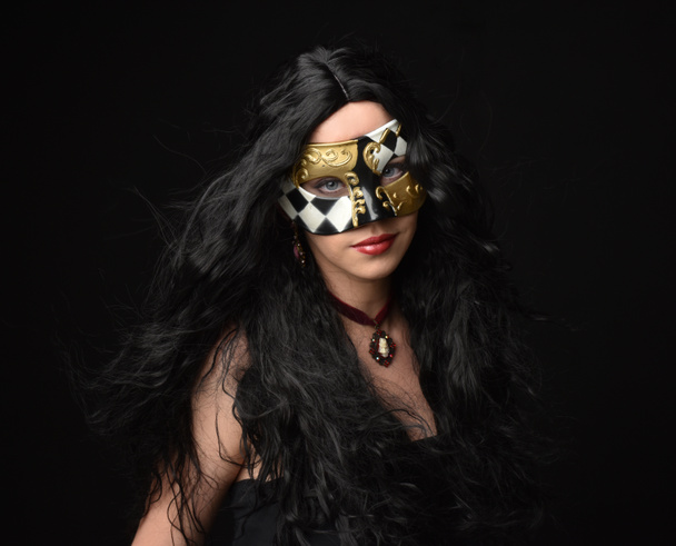 close up retrato de mulher bonita vestindo máscara de fantasia mascarada com longos cabelos pretos no fundo escuro estúdio. - Foto, Imagem