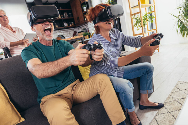 Grupo de amigos de mediana edad sonriendo felices jugando videojuegos con gafas VR en casa. - Foto, Imagen