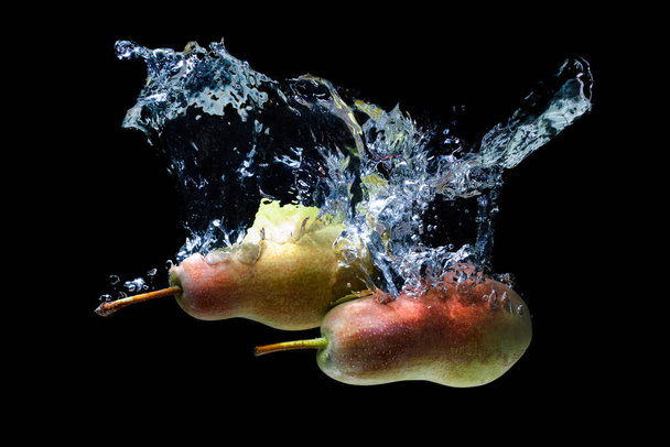 Two ripe whole pears dropped in water with splashes isolated on black background. - Foto, afbeelding
