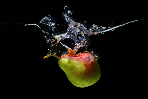 Ripe whole pear thrown in water with splashes isolated on black background. - Fotografie, Obrázek
