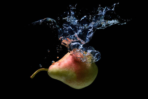 Ripe whole pear dropped in water with splashes isolated on black background. - Foto, afbeelding