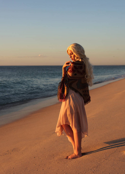 portrait pleine longueur de belle jeune femme aux cheveux longs portant une robe simple coulant dans le vent, pose élégante. fond de plage océan avec coucher de soleil doré éclairage. - Photo, image