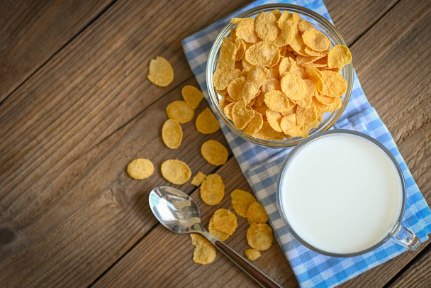 cornflakes mísa snídaně jídlo a svačinka pro zdravou stravu koncept, ranní snídaně čerstvé celozrnné cereálie, kukuřičné vločky s mlékem na dřevěném pozadí - pohled shora - Fotografie, Obrázek