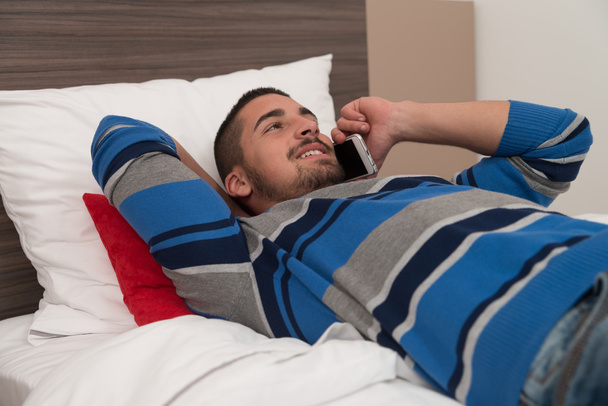 Happy Young Man Using Phone On Bed - Φωτογραφία, εικόνα