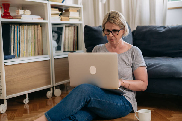 μέση ενήλικη γυναίκα που χρησιμοποιεί φορητό υπολογιστή στο σπίτι - Φωτογραφία, εικόνα