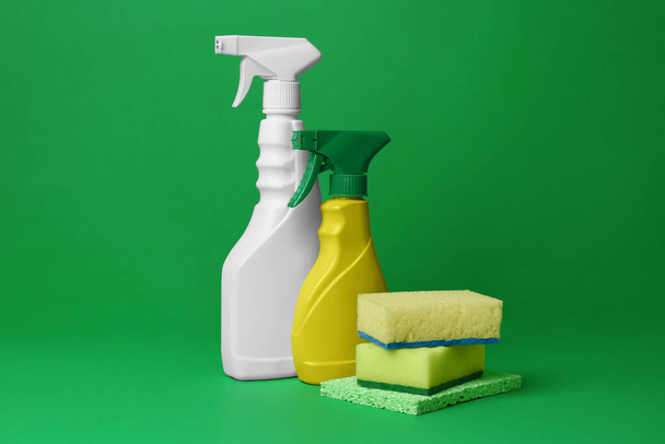Spray bottles of detergents and sponges on green background. Cleaning supplies - Foto, immagini