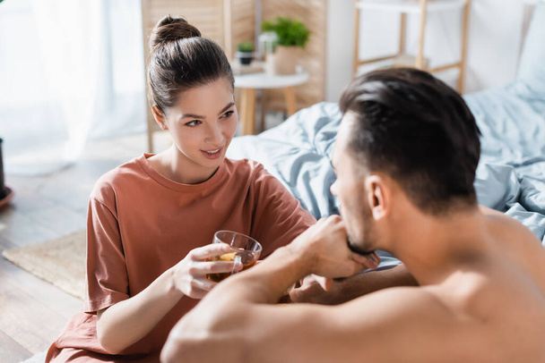smiling woman with tea cup talking to blurred boyfriend in bedroom - Foto, afbeelding