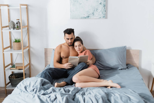 fiatal és szexi pár olvasás könyv szürke ágynemű otthon - Fotó, kép