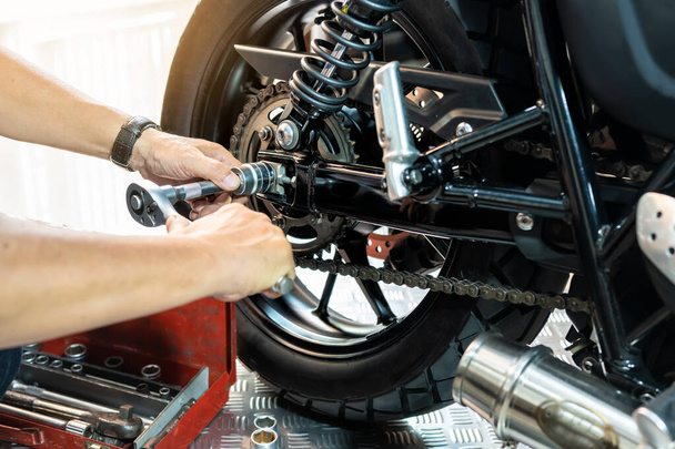 Mechanik pomocí klíče a zásuvky pro odstranění a výměnu zadního motocyklu kola, práce v údržbě garáže, opravy motocyklu konceptu.selektivní ostření - Fotografie, Obrázek