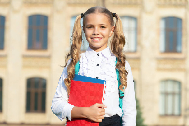 Happy teenage girl with pigtails in uniform holding school books outdoors, school. Back to school. Education and schooling. - Φωτογραφία, εικόνα