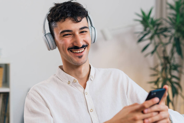 portrait of young adult man smiling, with headphones and holding mobile phone - Foto, afbeelding