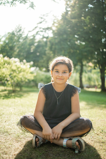 Yazlık parkta oturan gülümseyen küçük kızın açık hava portresi.. - Fotoğraf, Görsel