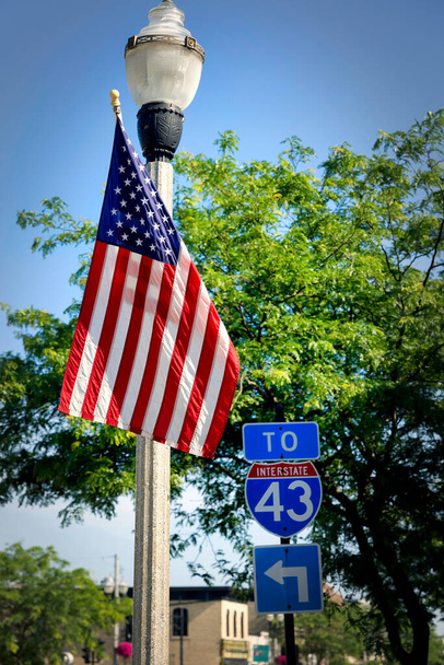 Eine amerikanische Flagge an einem Lichtmast steht neben einem Verkehrsschild für die I-43 in Two Rivers, Wisconsin. - Foto, Bild
