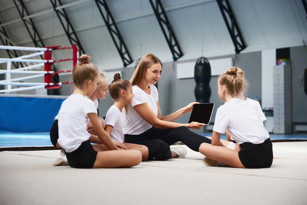 Coaching. Beginner gymnastics athletes doing exercises with gymnastics equipment at sports gym, indoors. Concept of achievements, studying, goals. Female coach training athletes - Foto, afbeelding