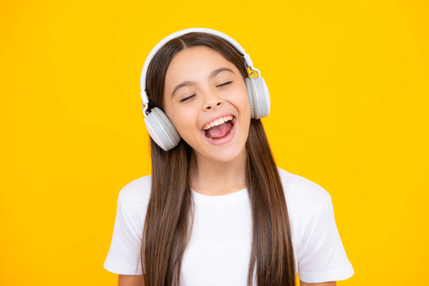 Teenager in modern wireless headphones enjoying song music in audio app, listening to her favorite music over yellow studio background - Фото, изображение