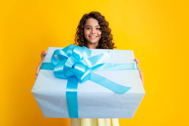 Happy teenager portrait. Child with gift present box on isolated studio background. Gifting for kids birthday. Smiling girl - Photo, image