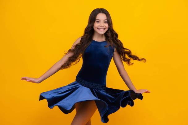 Happy girl face, positive and smiling emotions. Young graceful teenager child in fashion dress isolated on yellow background. Movement dress of young child girl. Beautiful teen in trendy clothing - Photo, Image