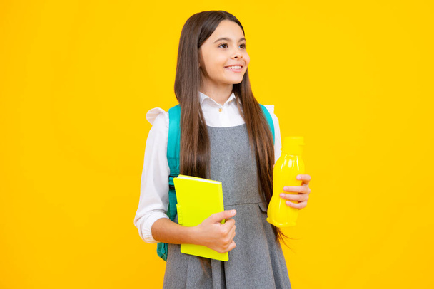 Teenager schoolgirl with backpack holding water bottle isolated on yellow background. Back to school concept. Healthy teen child - Фото, зображення