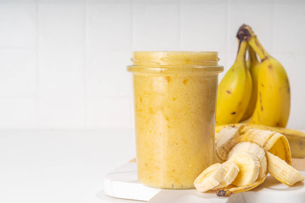 Bananas jam in small glass jar with fresh bananas on  white table background  - 写真・画像