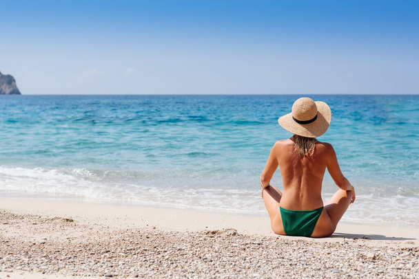 Korfu Yunanistan plajında saman şapkalı yeşil bikinili güzel sarışın kadın poz veriyor. Mutlu yaz tatilleri. - Fotoğraf, Görsel