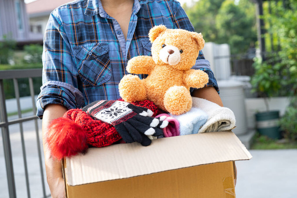 Tenue d'une boîte de don de vêtements avec des vêtements usagés et des poupées à la maison pour soutenir l'aide aux pauvres dans le monde. - Photo, image