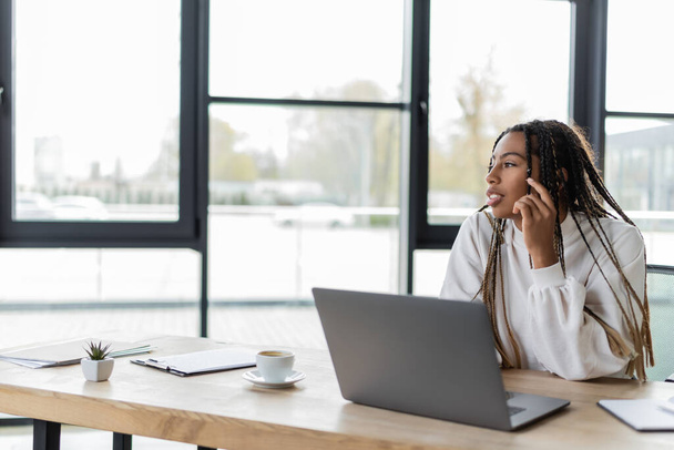African american businesswoman looking away near coffee and laptop in office  - Photo, Image