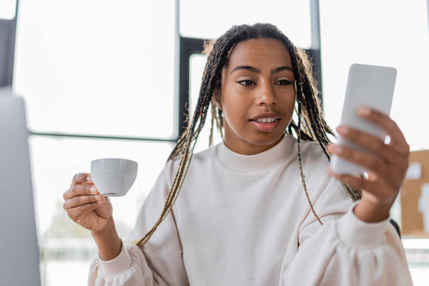 African american businesswoman using mobile phone and holding coffee cup in office  - Zdjęcie, obraz