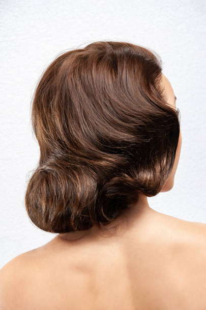 Back view of a young brunette woman. Portrait of a naked young white woman. Dark hair. Stylish hairstyle. Isolated on a light background - Photo, Image